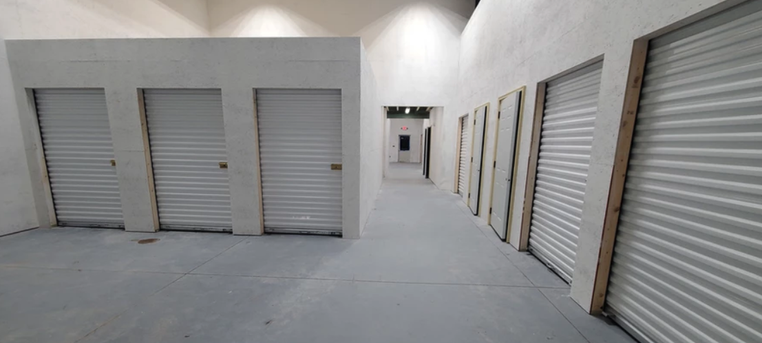 Indoor storage hallway with interior lighting, concrete flooring, and roll-up unit doors